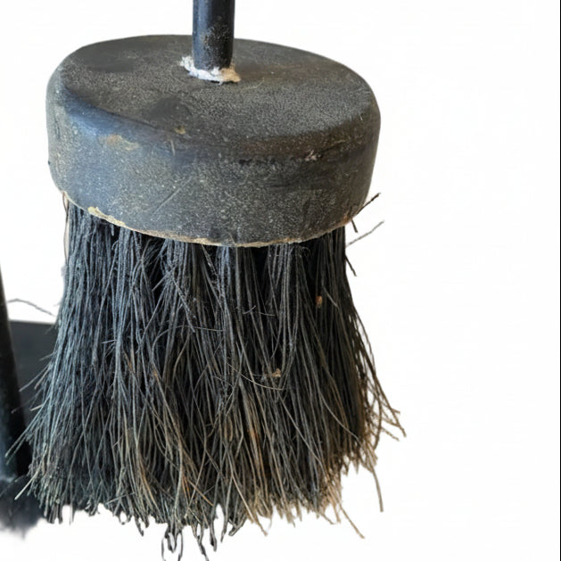 Black fireplace brush with bristles on a white surface