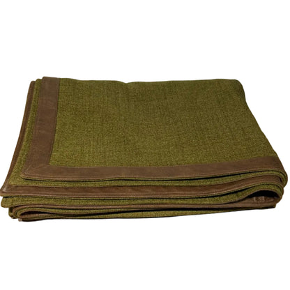 Folded green blanket with brown border on a wooden surface