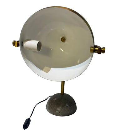 Lamp with a round white shade and gold accents on a textured white surface.