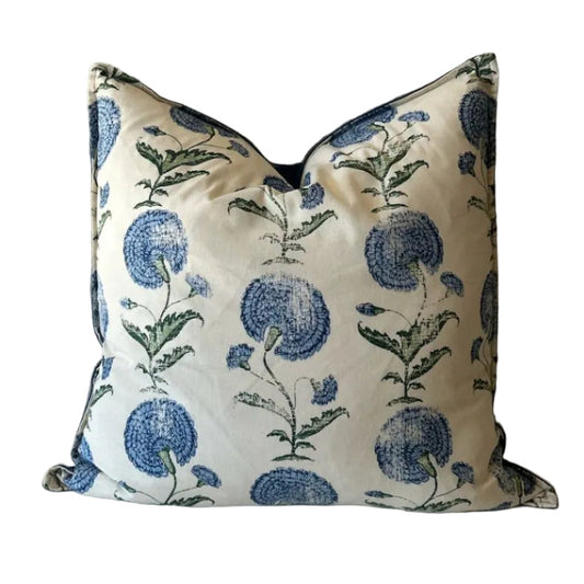 Decorative pillow with blue floral pattern on a white surface against a textured wall.