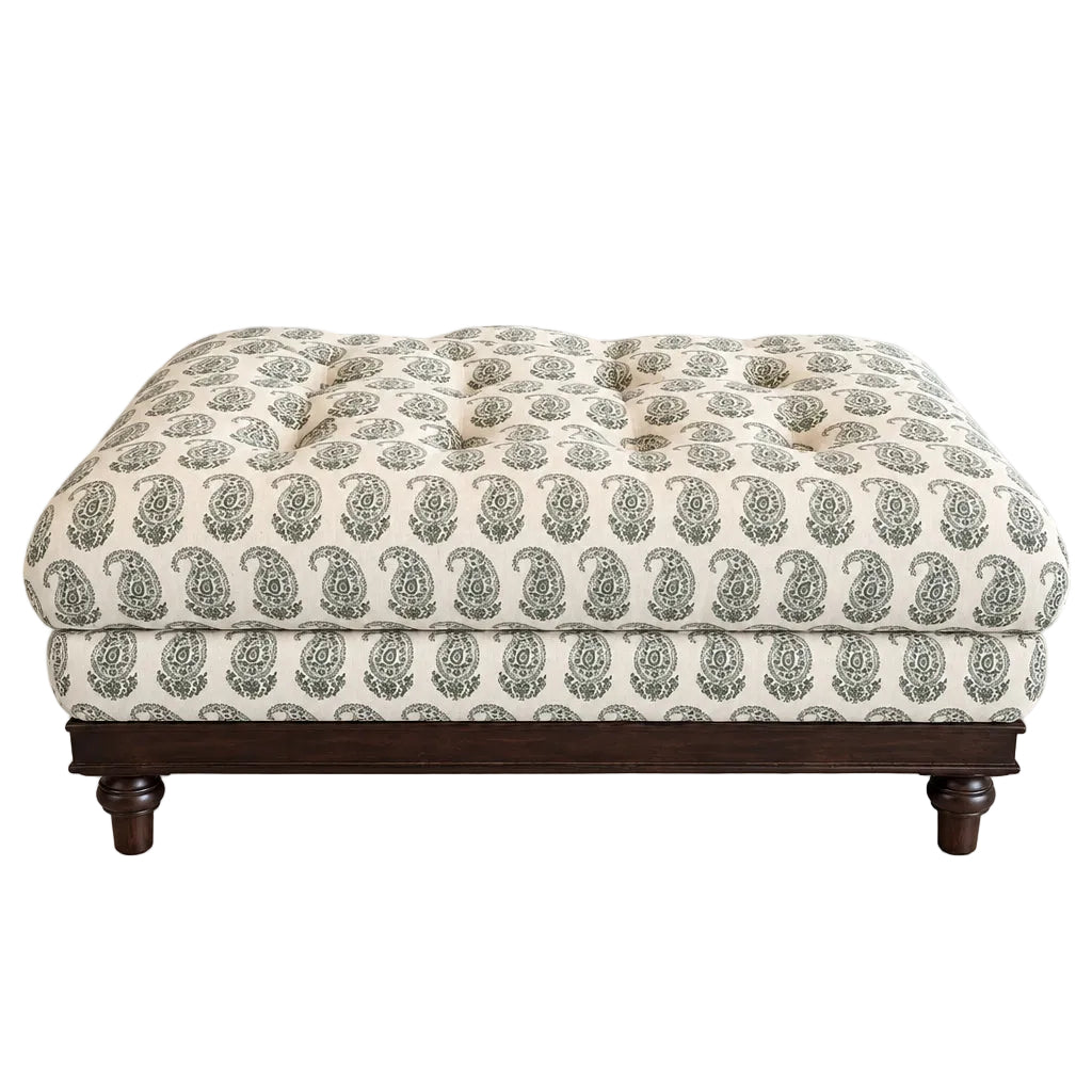 A tufted upholstered bench or ottoman with a cream fabric covered in a green paisley pattern, supported by a dark wood frame with turned legs